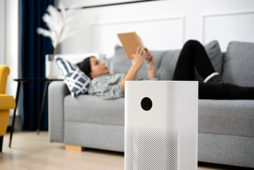 Closeup of an Air Purifier with a Woman Laying on Couch Reading a Book in the Background How to Improve Indoor Air Quality